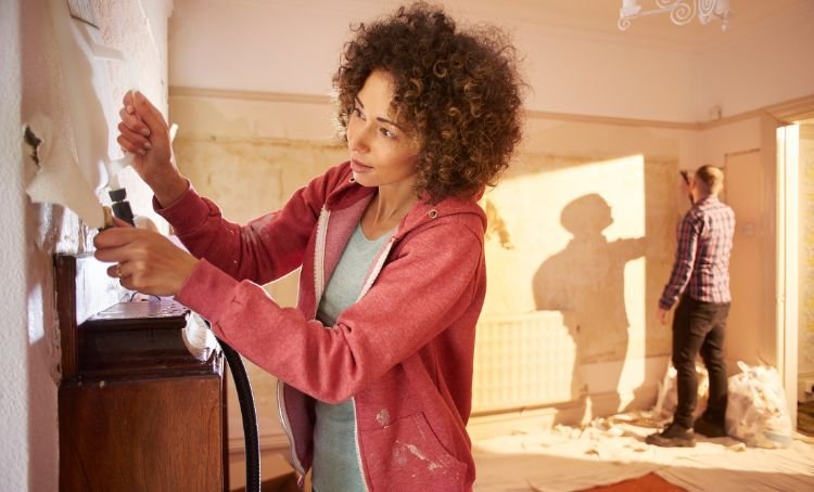 A woman stripping wallpaper in a fix and flip preoperty - ECF