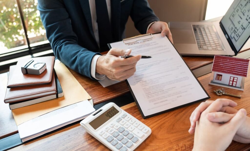 A man sitting at a desk with a laptop and calculator showing hte contents of a contract to a customer sitting opposite - Express Capital Financing