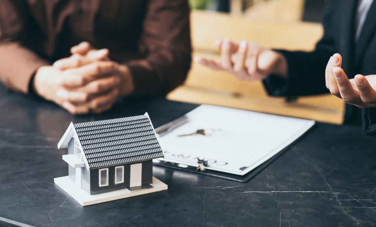 Two people at a desk with a small model house in the foreground and a contract on the desk - Express Capital Financing