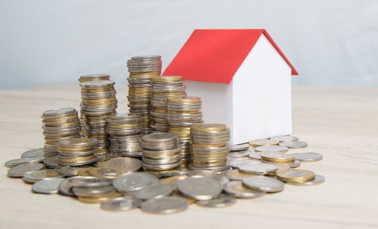 a small house beside a stack of coins - fix and flip property